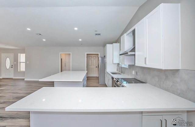 kitchen with sink, range, a center island, stainless steel refrigerator, and wall chimney range hood