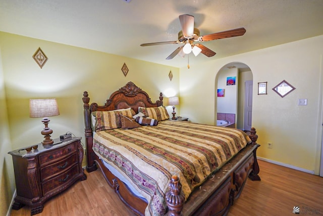 bedroom featuring baseboards, arched walkways, a ceiling fan, and wood finished floors