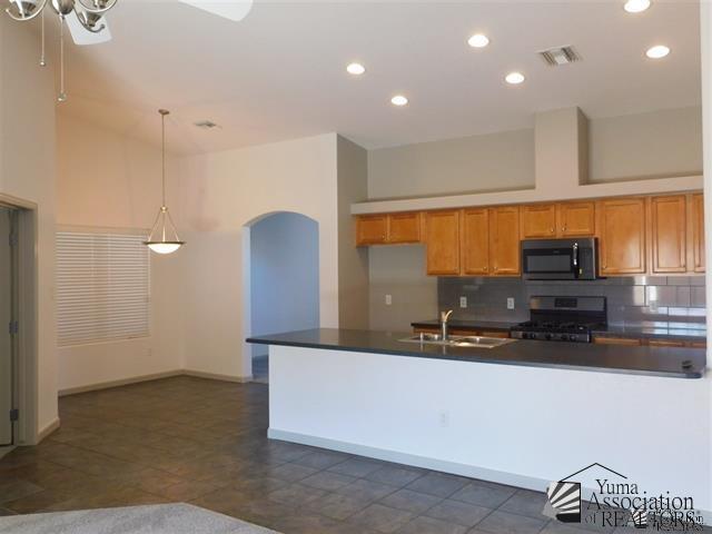 11785 E 27th Pl, Yuma, AZ 85367 - kitchen with black microwave, stainless steel gas stove, a sink, dark countertops, and brown cabinets