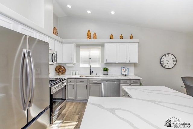 kitchen with backsplash, a sink, lofted ceiling, light wood-style floors, and stainless steel appliances