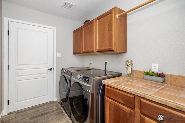 washroom with separate washer and dryer, cabinet space, wood finished floors, and visible vents