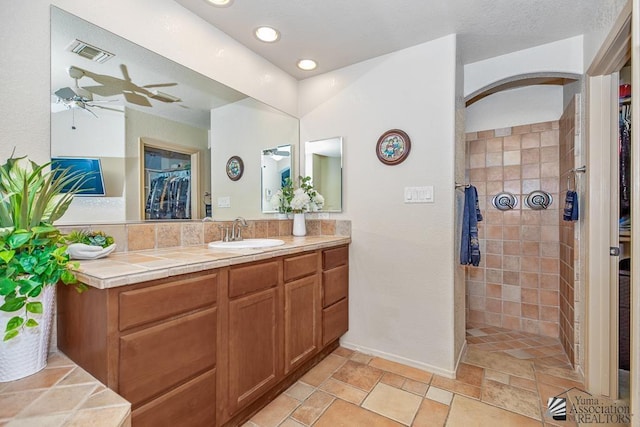 bathroom featuring a walk in shower, ceiling fan, vanity, a spacious closet, and visible vents