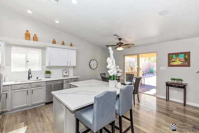 kitchen featuring ceiling fan, a sink, dishwasher, a kitchen breakfast bar, and decorative backsplash