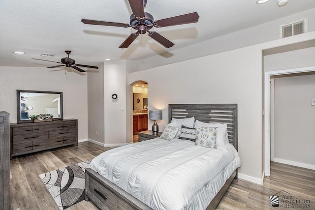 bedroom featuring visible vents, wood finished floors, baseboards, ceiling fan, and arched walkways