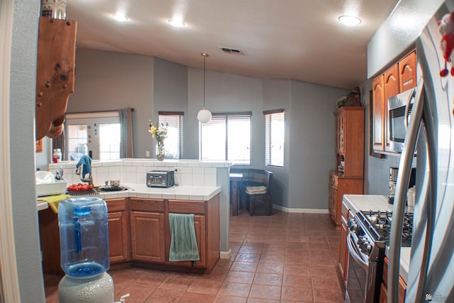 kitchen featuring tile counters, vaulted ceiling, stainless steel appliances, and visible vents