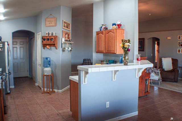 kitchen featuring brown cabinets, arched walkways, a kitchen breakfast bar, tile countertops, and a peninsula