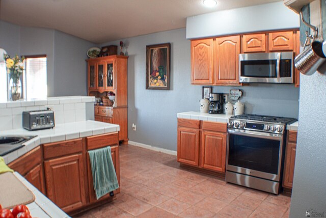 kitchen with tile counters, baseboards, appliances with stainless steel finishes, and light tile patterned floors