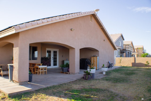 rear view of property with fence, stucco siding, french doors, a patio, and a yard