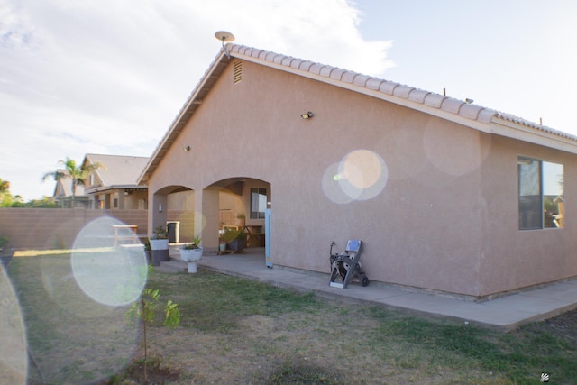 rear view of house with stucco siding, a patio area, and fence