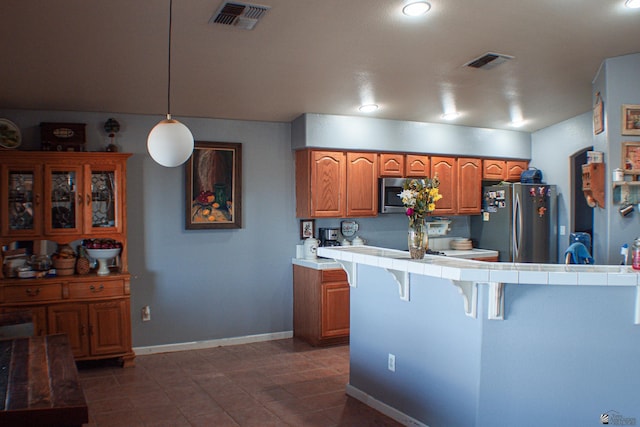 kitchen featuring visible vents, a breakfast bar area, tile countertops, brown cabinets, and appliances with stainless steel finishes