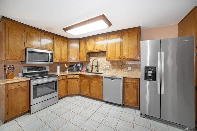 kitchen featuring stainless steel appliances, a sink, brown cabinetry, and light countertops