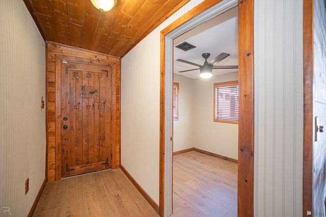 corridor with light wood-type flooring, baseboards, wooden ceiling, and wooden walls