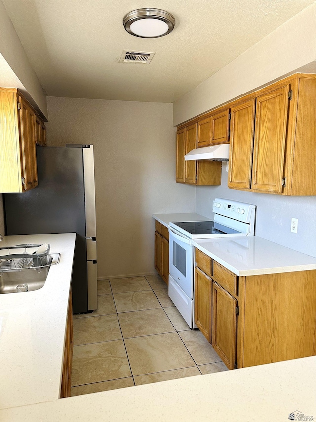 4732 W 17th Ln, Yuma, AZ 85364 - kitchen with white range with electric cooktop, under cabinet range hood, freestanding refrigerator, light countertops, and brown cabinets