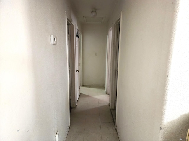 corridor with light tile patterned floors and attic access