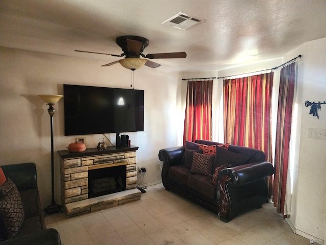 living room featuring ceiling fan, a stone fireplace, and visible vents