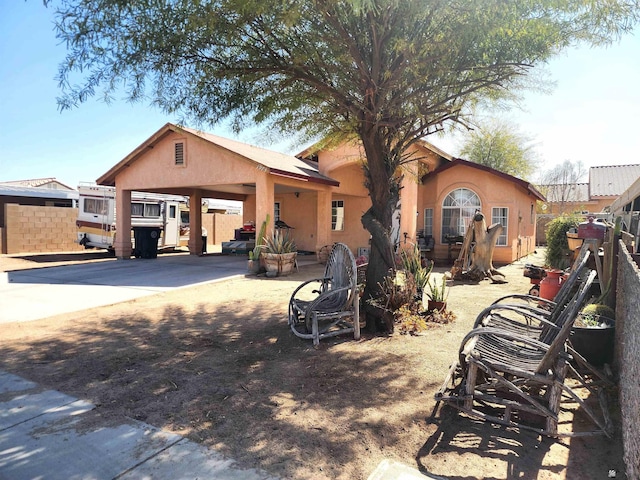 view of front of property featuring driveway, fence, a carport, and stucco siding