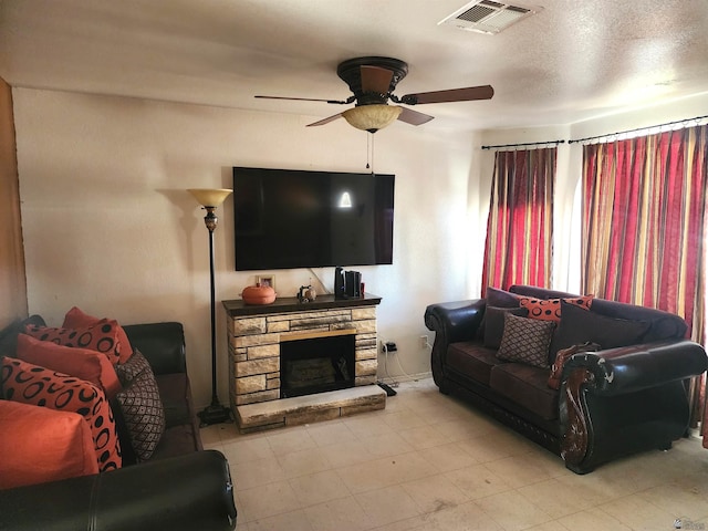 living area with visible vents, ceiling fan, a stone fireplace, and a textured ceiling