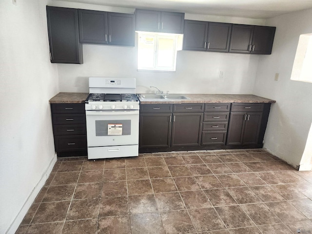 kitchen with stone finish flooring, baseboards, a sink, and gas range gas stove
