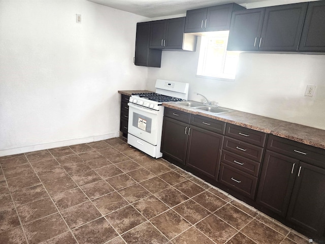 kitchen with a sink, baseboards, and white range with gas cooktop