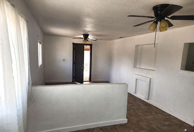 interior space featuring baseboards, a textured ceiling, ceiling fan, and visible vents