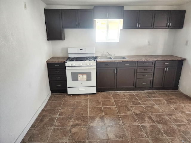 kitchen with a sink, baseboards, white gas range oven, and stone finish flooring