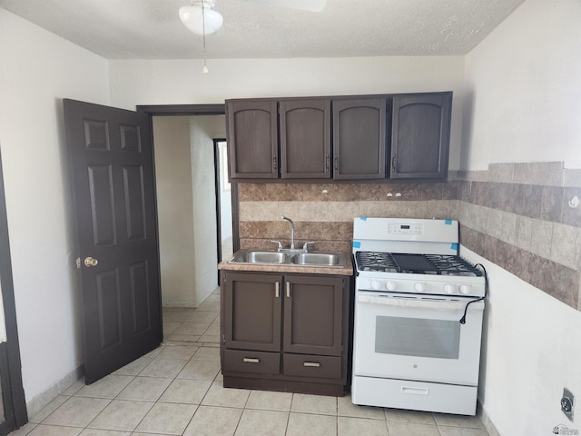 kitchen with dark brown cabinets, light tile patterned floors, white range with gas stovetop, and a sink