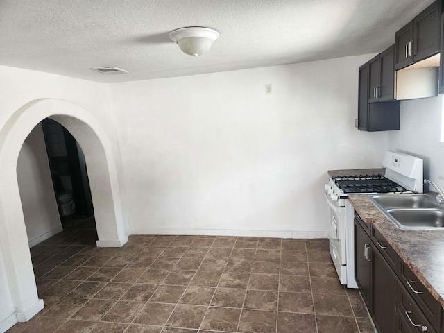 kitchen featuring a sink, arched walkways, a textured ceiling, white gas range, and baseboards