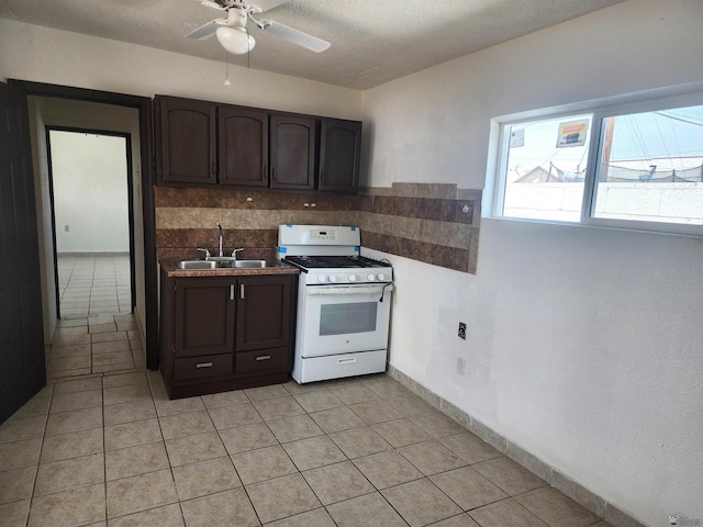 kitchen featuring white gas range, ceiling fan, dark countertops, a sink, and light tile patterned flooring