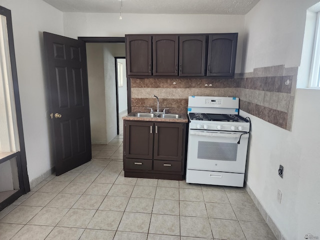 kitchen featuring gas range gas stove, a sink, light tile patterned floors, and dark brown cabinetry
