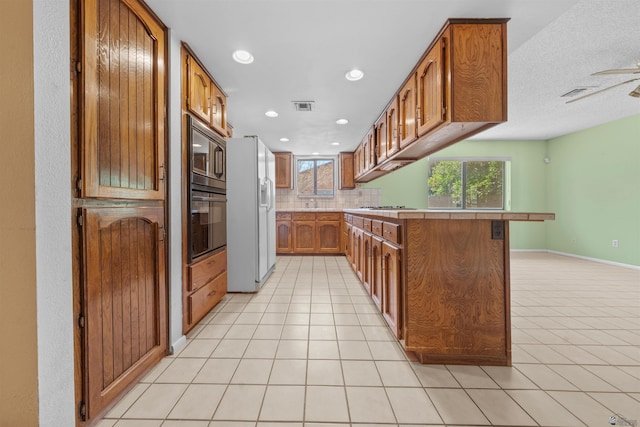 1228 S 40th Dr, Yuma, AZ 85364 - kitchen featuring white refrigerator with ice dispenser, black oven, light tile patterned floors, brown cabinets, and recessed lighting