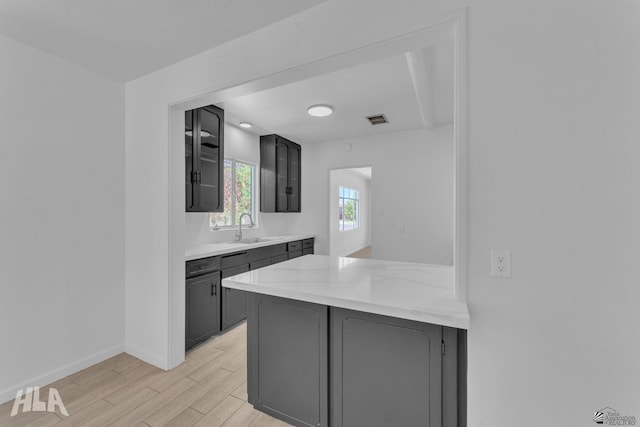kitchen featuring a sink, light wood finished floors, a peninsula, visible vents, and glass insert cabinets