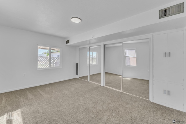 unfurnished bedroom featuring multiple closets, multiple windows, carpet floors, and visible vents