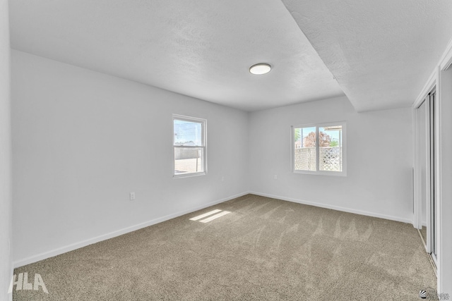 unfurnished bedroom featuring a textured ceiling, multiple windows, baseboards, and carpet