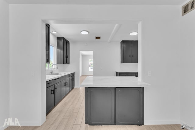 kitchen featuring a sink, light wood finished floors, light countertops, baseboards, and visible vents