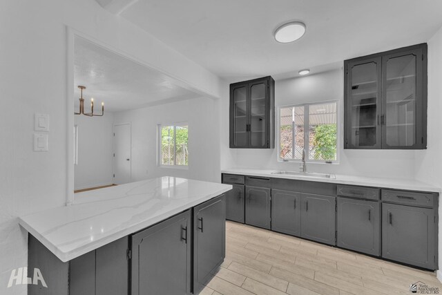 kitchen featuring light wood-style floors, an inviting chandelier, a sink, gray cabinetry, and glass insert cabinets