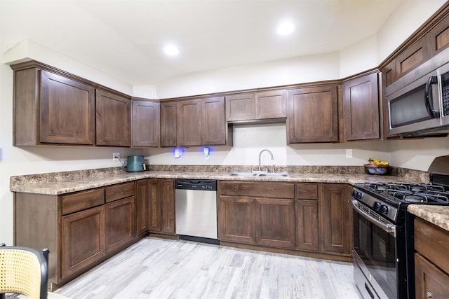 kitchen with appliances with stainless steel finishes, a sink, dark brown cabinets, light wood finished floors, and recessed lighting