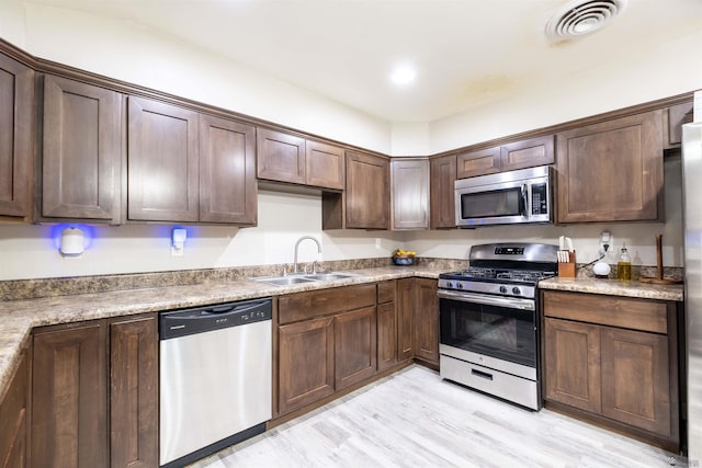kitchen with stainless steel appliances, a sink, light wood finished floors, and dark brown cabinets