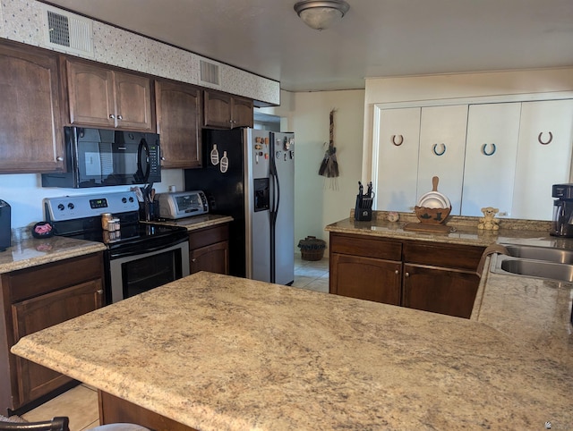 kitchen with sink, light tile patterned floors, appliances with stainless steel finishes, dark brown cabinetry, and kitchen peninsula