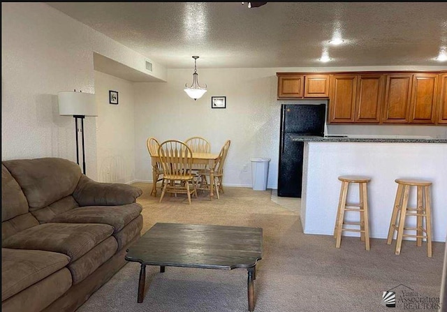kitchen featuring freestanding refrigerator, light carpet, brown cabinetry, open floor plan, and a breakfast bar area