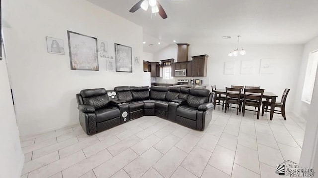 living area with ceiling fan with notable chandelier, light tile patterned flooring, and vaulted ceiling