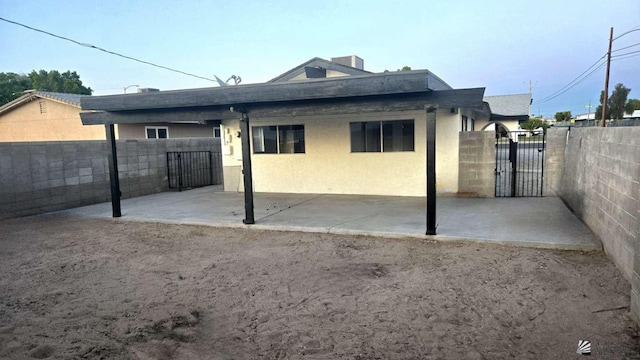rear view of house featuring a patio, a gate, fence, and stucco siding