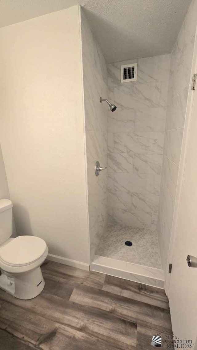 full bathroom with a textured ceiling, visible vents, a shower stall, wood finished floors, and toilet