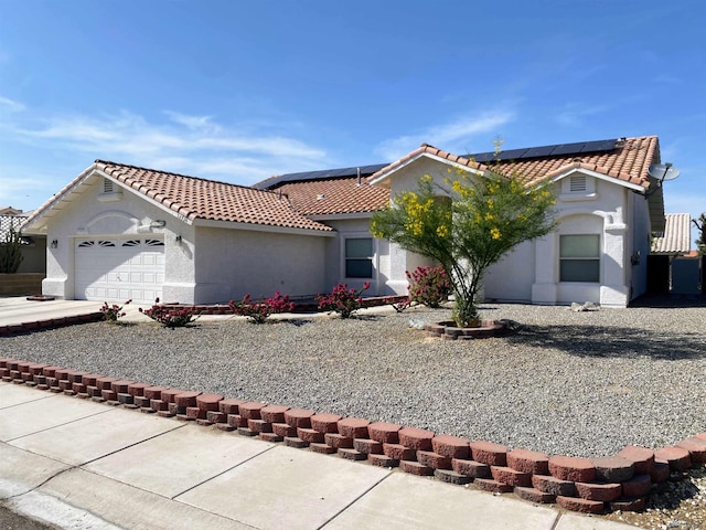mediterranean / spanish-style house with a garage, stucco siding, a tiled roof, and solar panels
