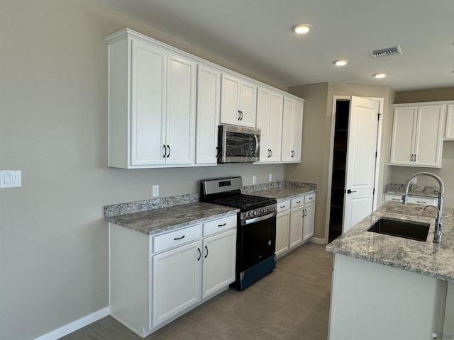 kitchen featuring black gas range, light stone countertops, sink, and white cabinets