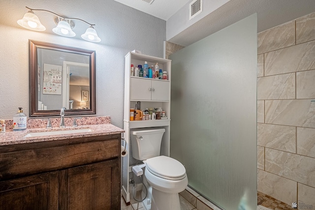 full bath with vanity, a tile shower, toilet, and visible vents