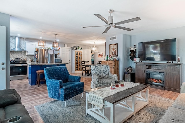 living area with a ceiling fan, visible vents, a glass covered fireplace, and light wood finished floors