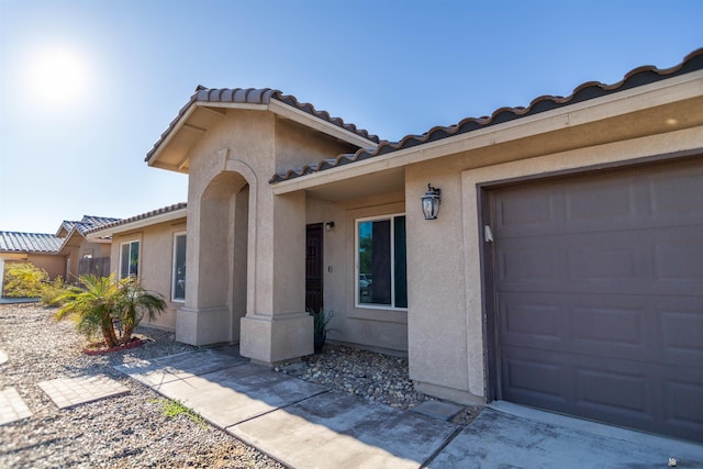 view of exterior entry with stucco siding, a tile roof, and an attached garage