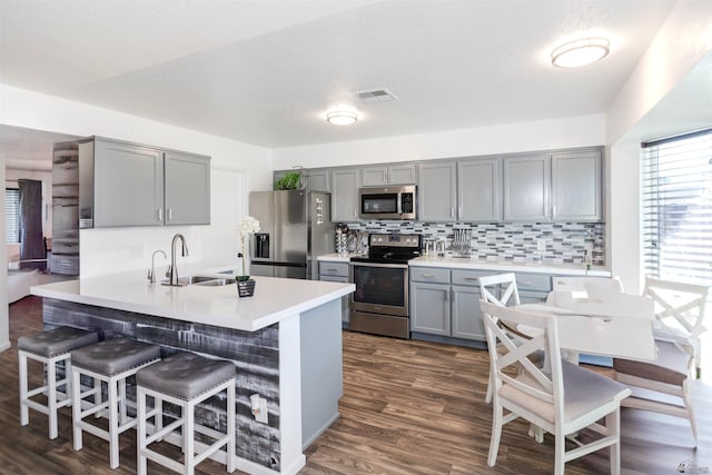 kitchen featuring stainless steel appliances, gray cabinets, a sink, a breakfast bar area, and backsplash