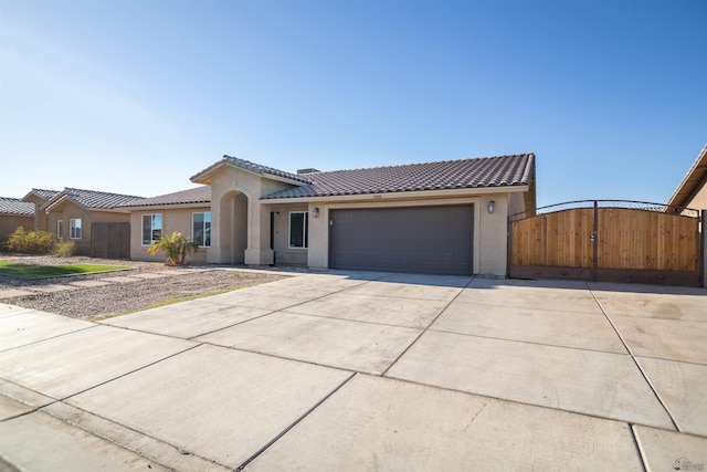 view of front of house with an attached garage, a tiled roof, driveway, stucco siding, and a gate