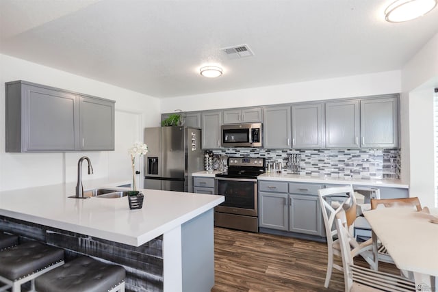 kitchen featuring appliances with stainless steel finishes, gray cabinets, a sink, a breakfast bar, and dark wood-style floors